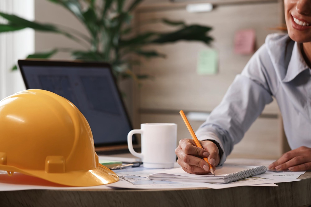 Personne écrivant près d'un casque de chantier jaune.